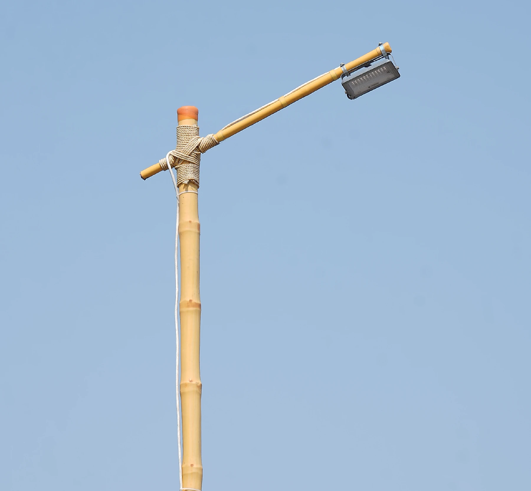 Close-up of an LED fixture mounted on a bamboo light pole against a clear blue sky